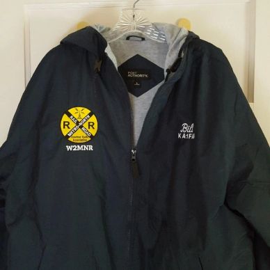 Black jacket with yellow railroad logo and text, hanging on a hanger.