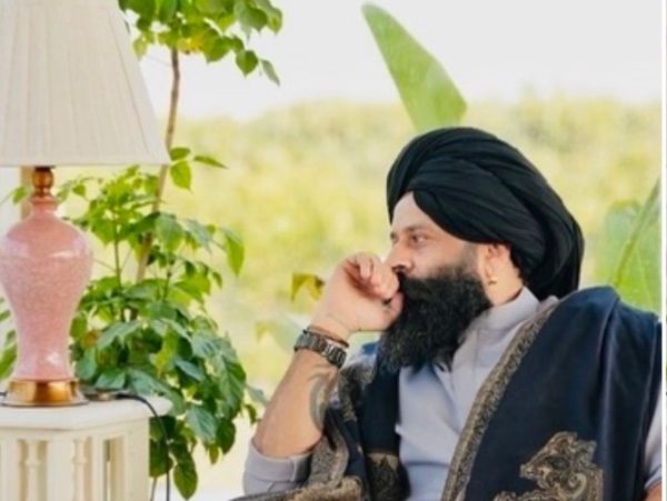 Man in traditional attire sitting pensively near a lamp and plant.