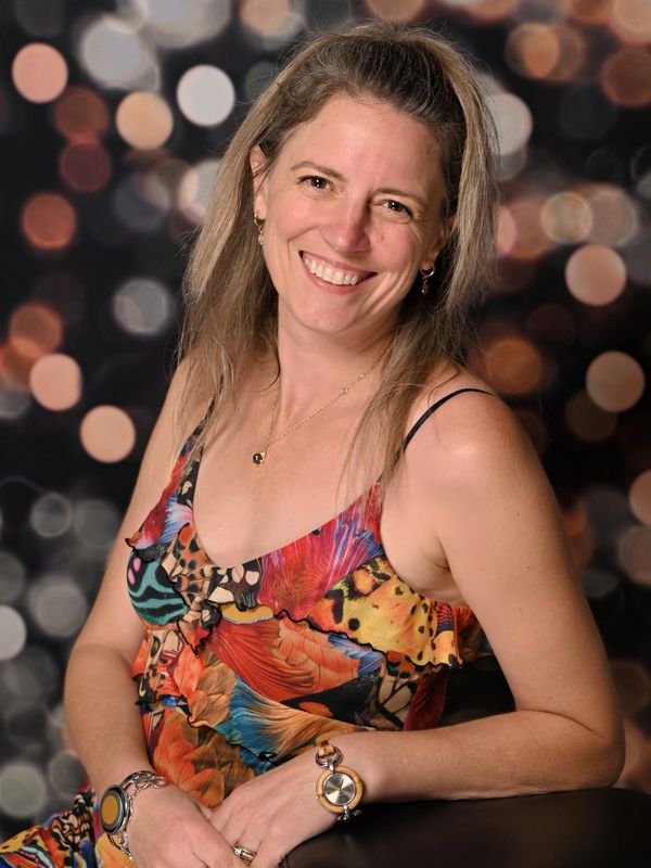 Femme souriante en robe colorée devant un fond flou.