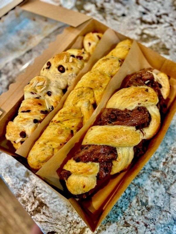 Three braided pastries with different fillings in a box on a granite countertop.