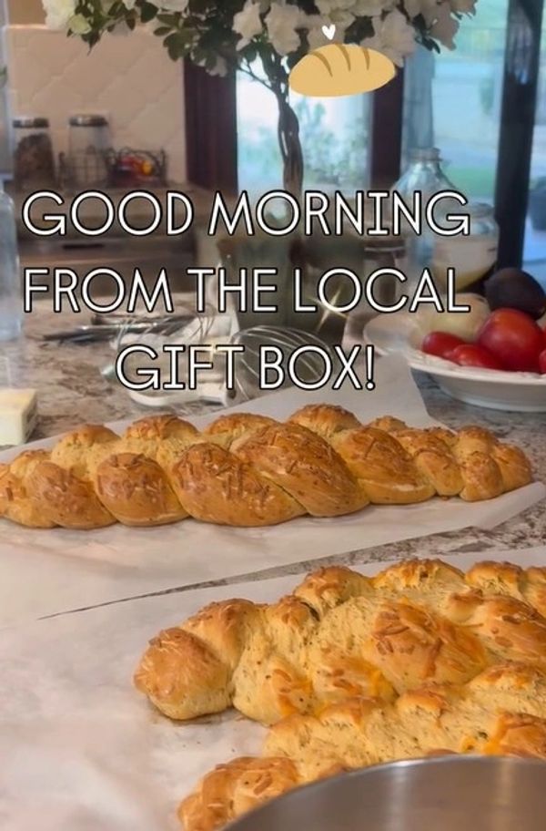 Freshly baked braided bread on a kitchen counter with flowers and fruit bowl.