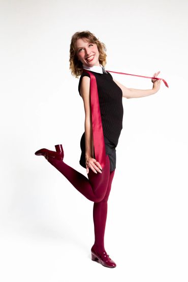Smiling woman poses playfully with one leg raised, wearing black and burgundy outfit.