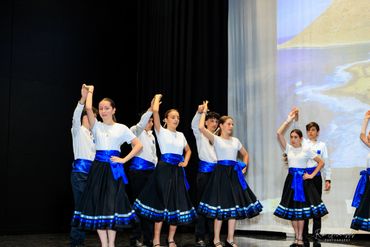 Young dancers performing a traditional folk dance in coordinated blue and black costumes.