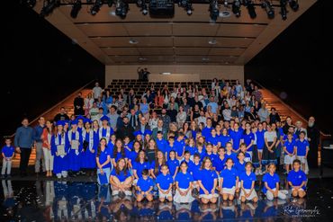 Large group of students, graduates, and adults posing indoors on a stage.