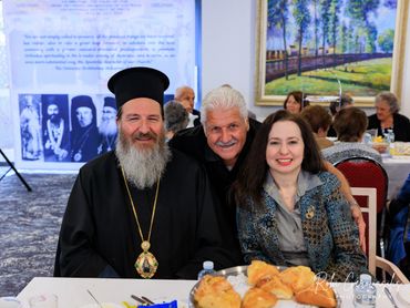 Three smiling people at a festive gathering, including a man in religious attire.