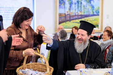 A joyful man in religious attire hands a paper to a smiling woman holding a basket.