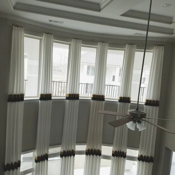 Floor-to-ceiling curtains with gold and black bands adorn a curved window wall.