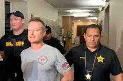 A man is escorted by two sheriff officers in a hallway.