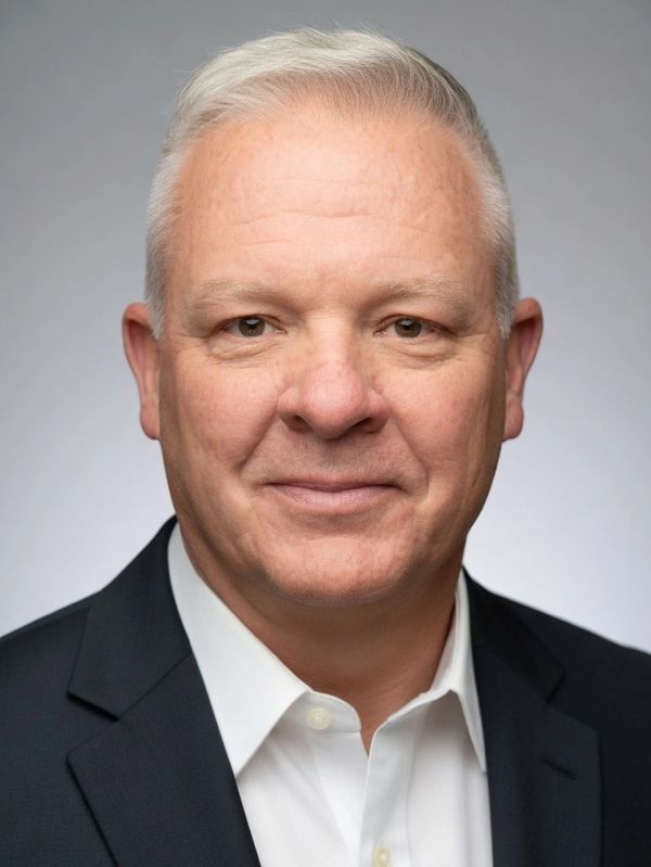 Professional headshot of a middle-aged man in business attire with a neutral background.