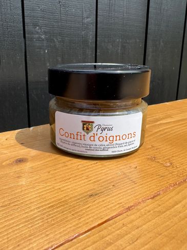 A jar of Domaine Pyrus Confit d'oignons placed on a wooden surface against a black wooden background.