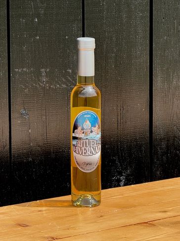 A tall bottle of golden liquid labeled Rituel Hivernal on a wooden surface.