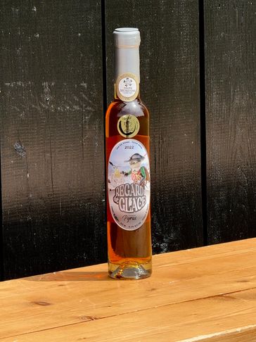 Tall bottle of Regard Glacé liqueur on a wooden surface against a dark background.