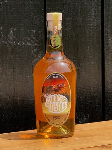 A bottle of Carrosse du Diable Pyrus with amber liquid on a wooden surface.