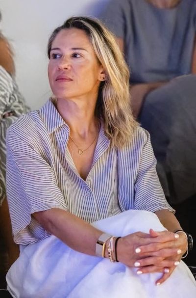 Woman in a striped shirt sitting with hands clasped, looking to the side.
