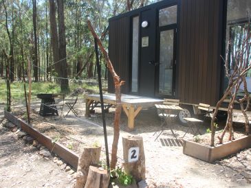 A small cabin in the woods with outdoor seating and a fire pit.