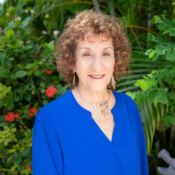 Merle R. Saferstein in a blue blouse standing in front of greenery.