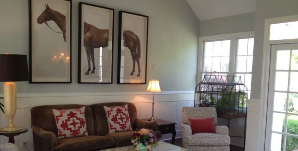 Living room couch, red & white pillows, three pictures above show head, middle and end of a horse. 