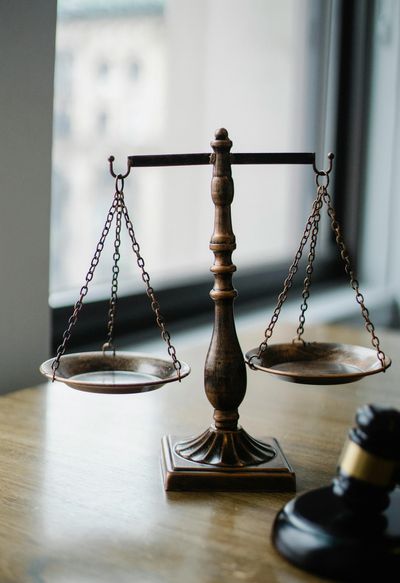 Wooden balance scale and gavel on a desk near a window.