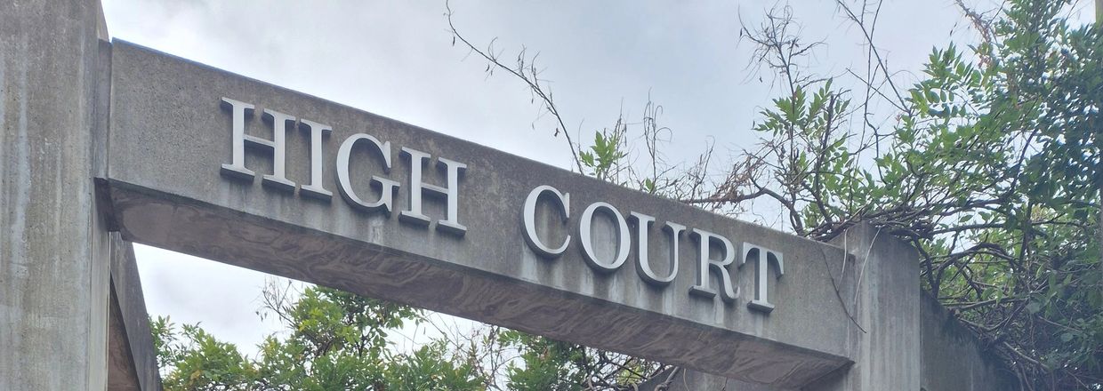 Concrete archway with 'HIGH COURT' sign surrounded by greenery.