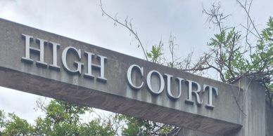 Stone entrance sign reading 'HIGH COURT' with trees in the background.