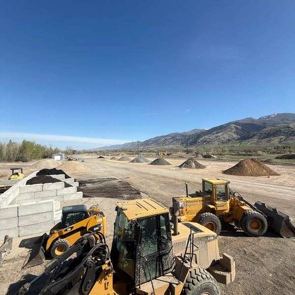 Construction site with heavy machinery and dirt piles under a clear blue sky.