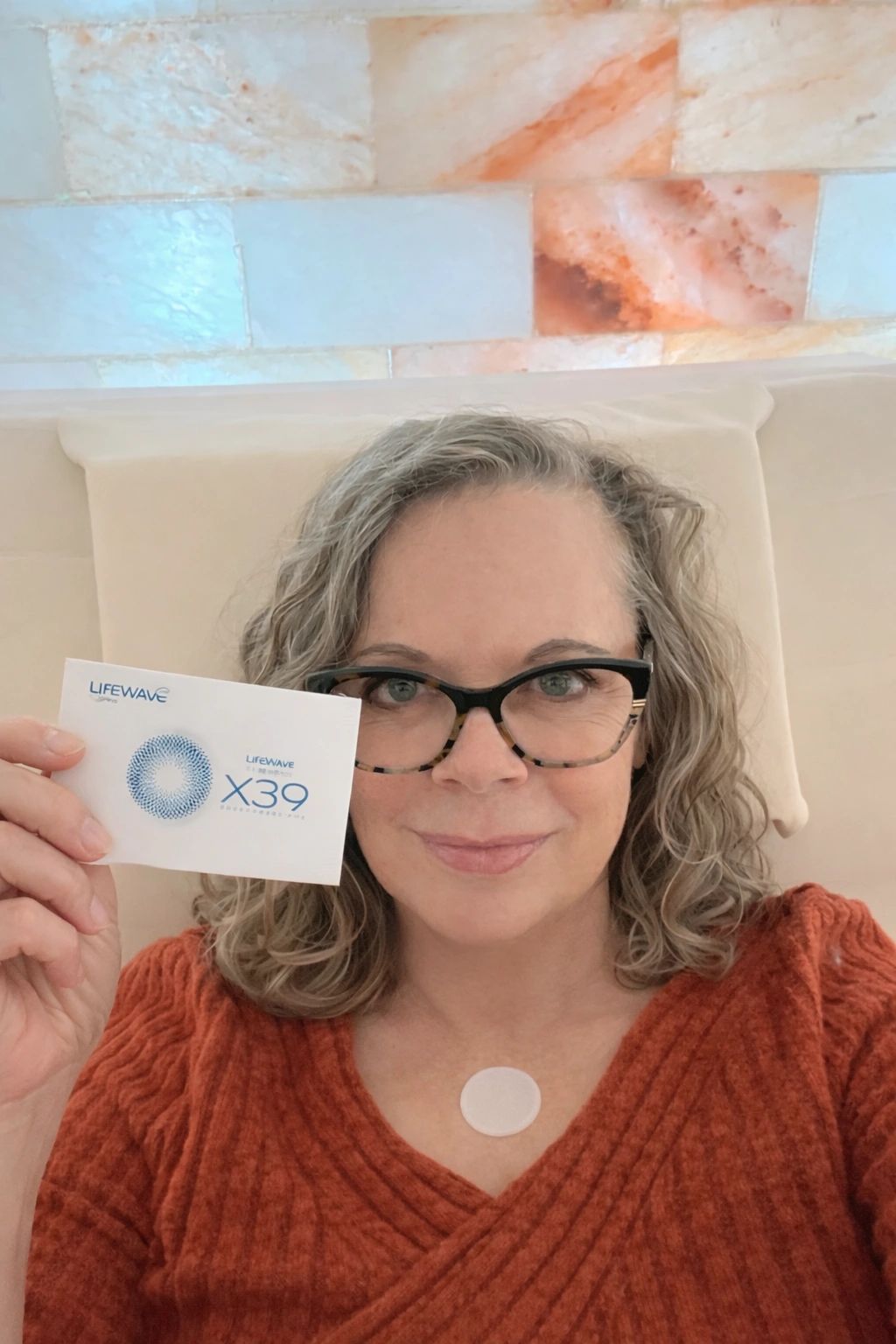 Woman holding a LifeWave X39 patch packet with a patch on her chest, smiling.