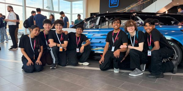 Group of young people posing in front of a blue car indoors.