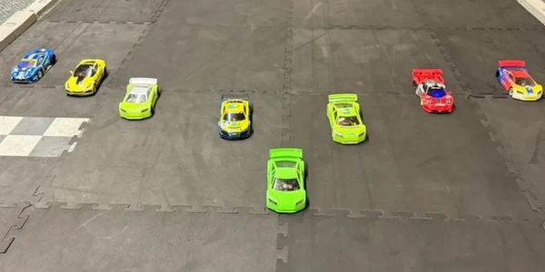 Seven colorful toy race cars lined up on a black track, ready to race.