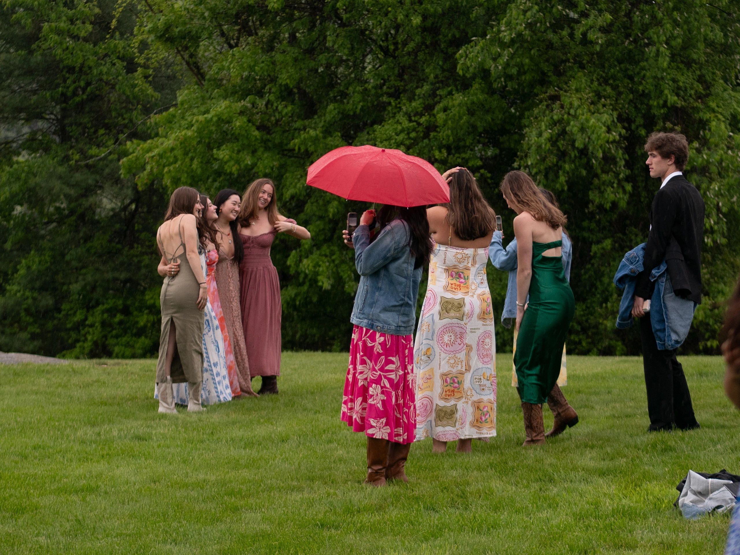 Group of young friends posing for photos outdoors in dresses and suits.