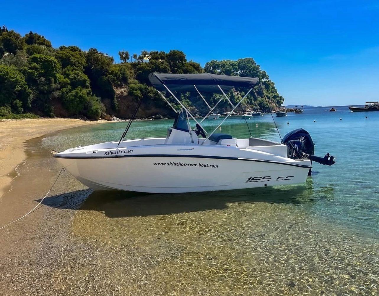 Small white motorboat anchored near a sandy beach with clear water.