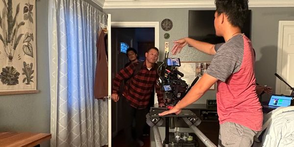 Two men enter a room while a cameraman films them.