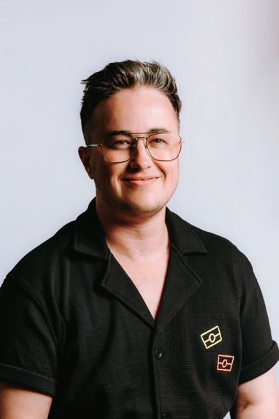 Jack is white skinned, has short brown and grey hair and is wearing glasses and a black shirt.