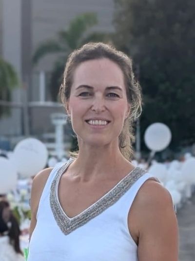 Smiling woman in white dress with silver trim at an outdoor event.