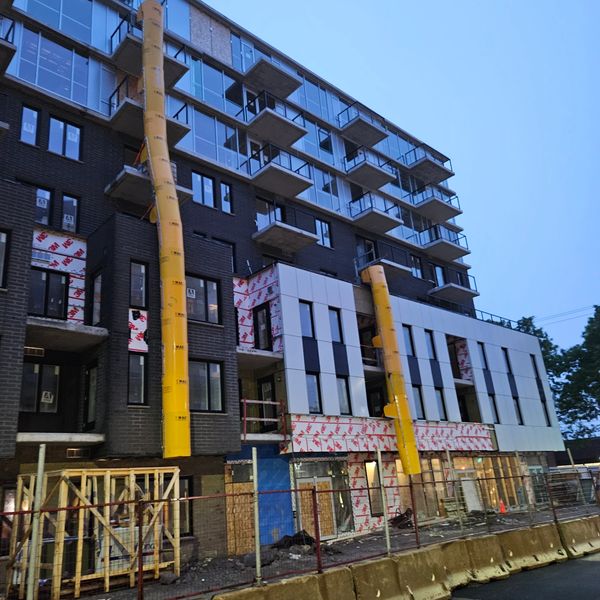 A mid-rise building under construction with yellow debris chutes and glass balconies.