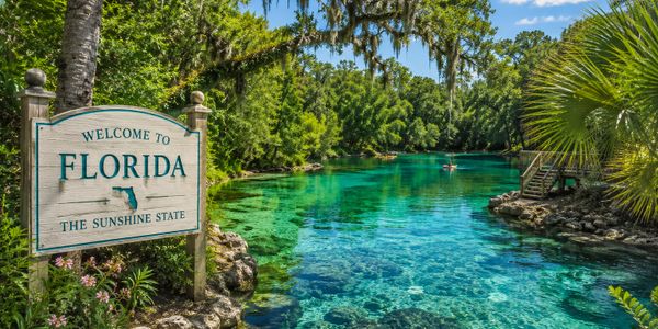 Welcome sign by a clear blue river in lush Florida nature.