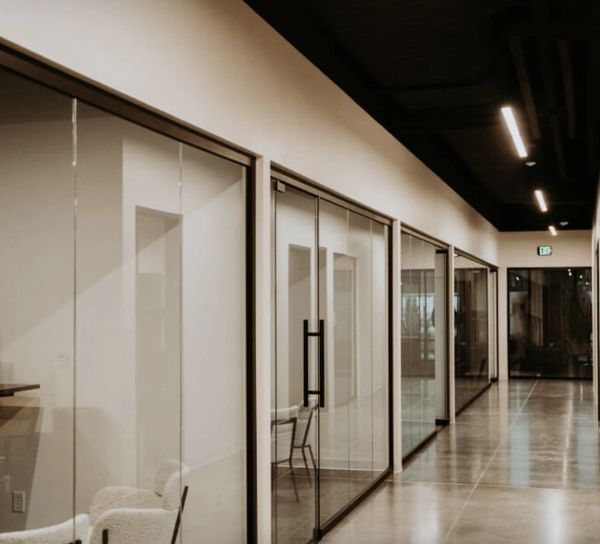 Modern office hallway with glass-walled rooms and polished concrete floors.