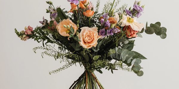 A rustic bouquet of mixed flowers with green foliage against a light background.