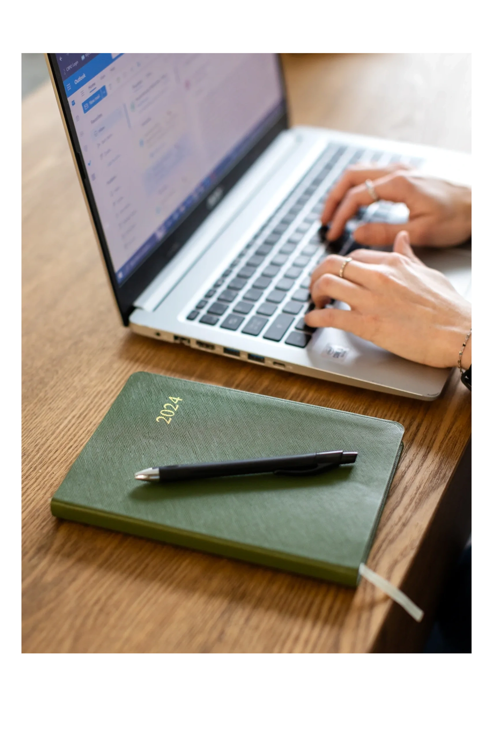 Hands typing on laptop next to planner and pen.