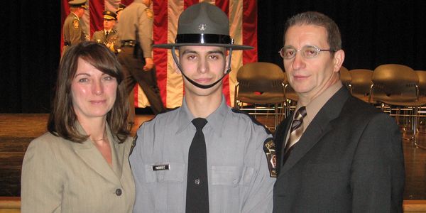 Young cadet in uniform poses with two adults at a formal event.