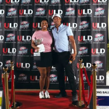 Two people posing on a red carpet with a trophy.