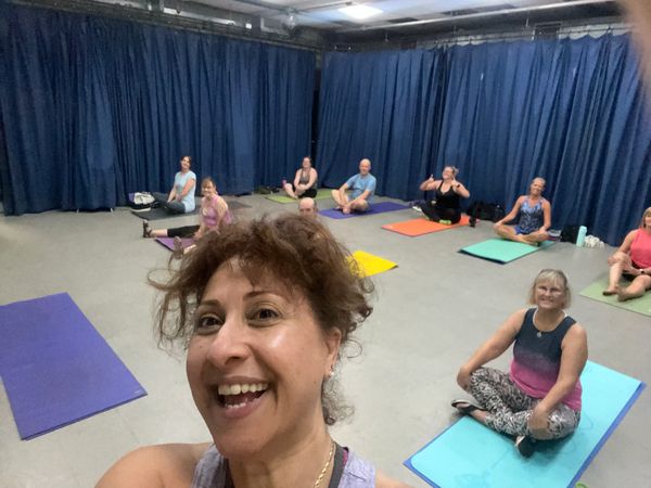 Group yoga class with participants smiling on mats.