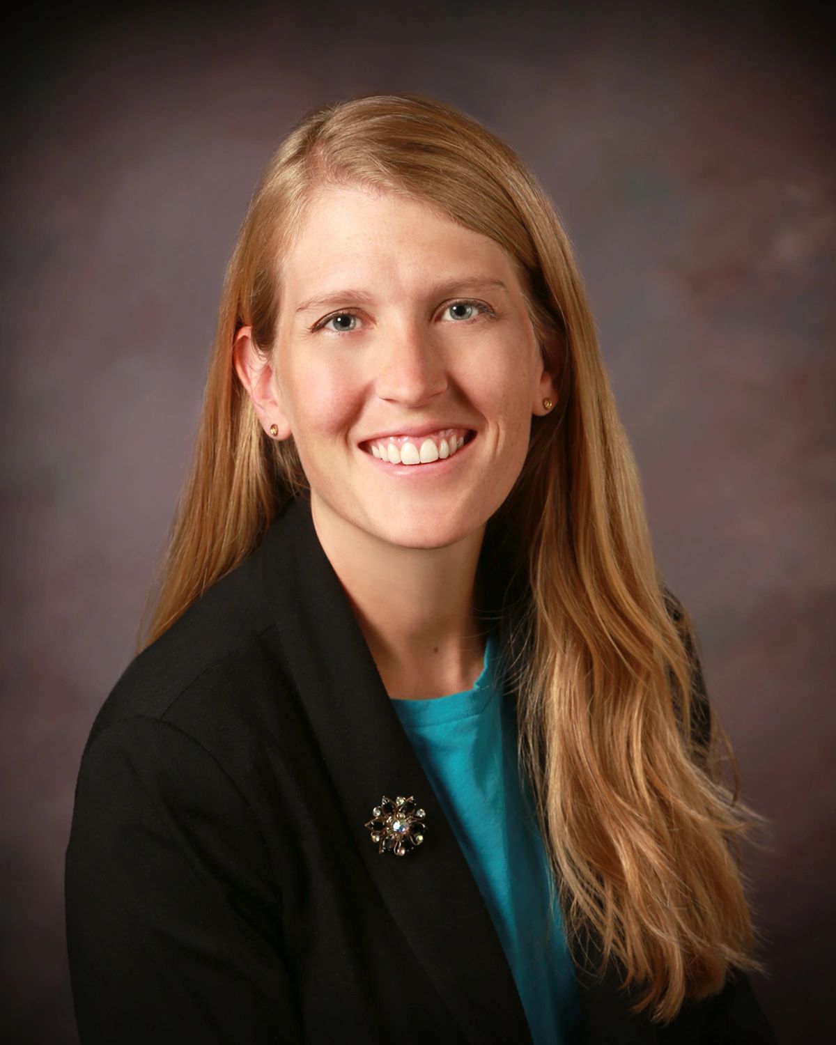 Photo of Elizabeth smiling at the camera. She has long blonde hair and is wearing blue shirt, black 