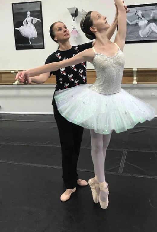 Ballet teacher guiding a young ballerina in a dance studio.