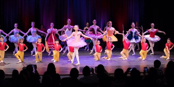 Young ballet dancers performing on stage with colorful costumes and an audience watching.