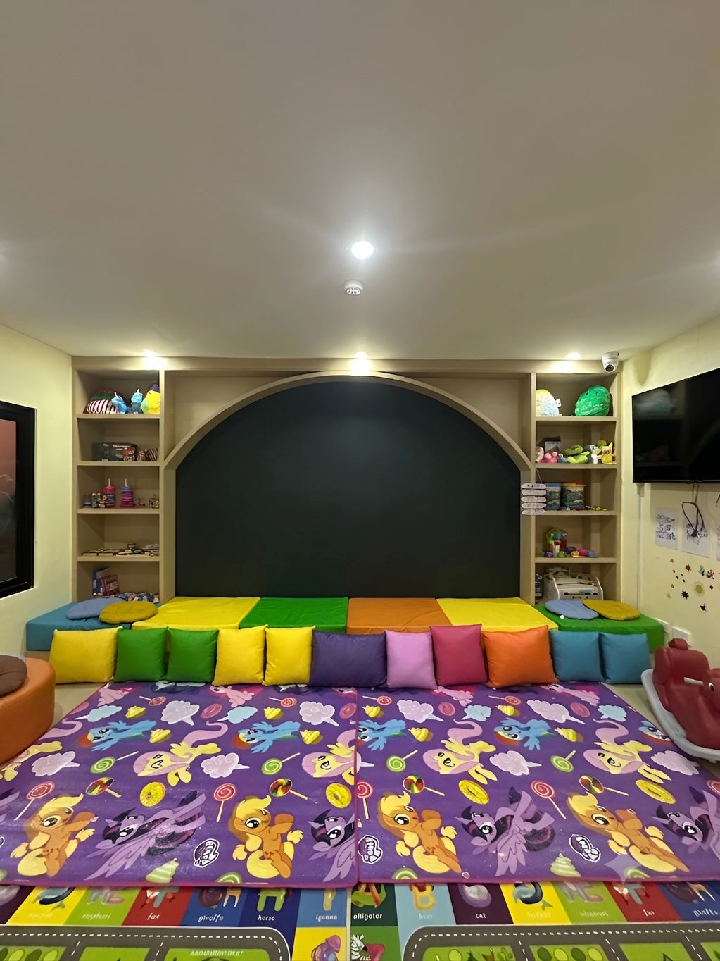 Colorful kids' playroom with cushions, toys, and a TV.