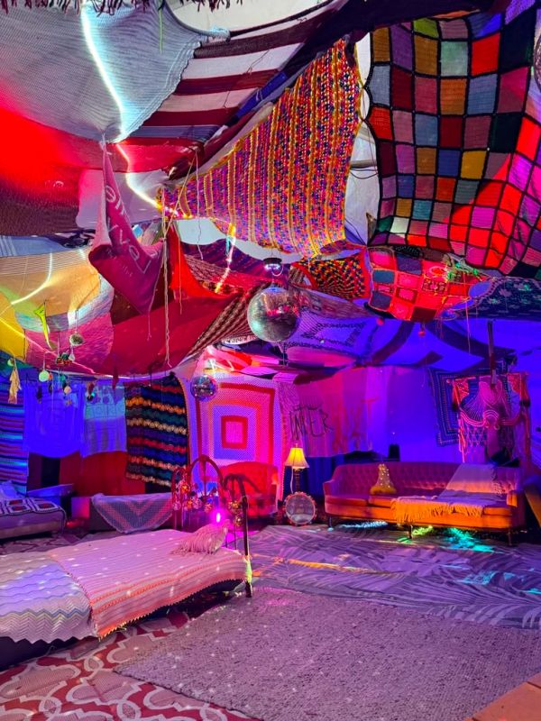 Colorful bohemian room with fabric-covered ceiling and cozy seating.