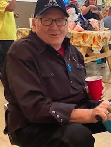 Elderly man smiling, holding a red cup at a casual indoor gathering.