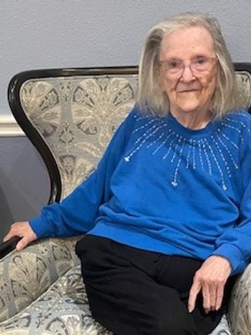 Elderly woman sitting comfortably on a patterned armchair.