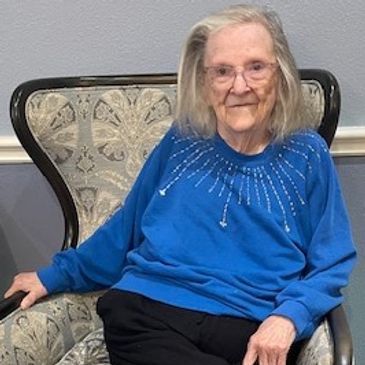 Elderly woman sitting comfortably on a patterned armchair.