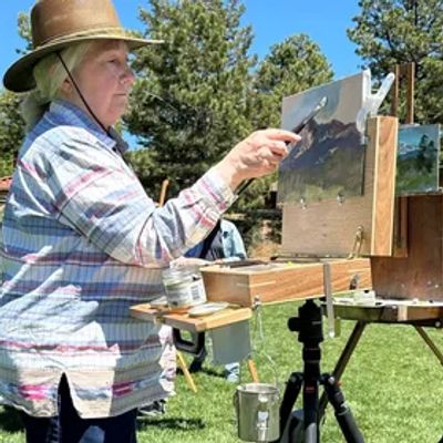 Artist painting outdoors with a mountain landscape.
